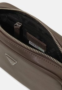 Borsa sintetica marrone con esterno testurizzato, interno nero, cerniera argentata e etichetta GUESS ECO all'interno. Presenta una piccola tasca interna.