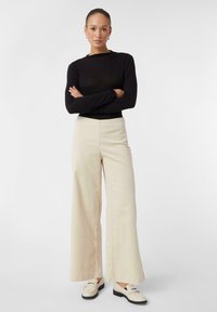 Czarna bluzka z długim rękawem w połączeniu z szerokimi beżowymi spodniami i kremowymi loaferami. Spodnie mają gładką teksturę i wysoką talię.