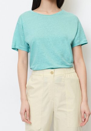 Turkis bomuld t-shirt med rund halsudskæring og korte ærmer, båret med cremefarvede, højttaljede bukser med knaplukning.