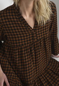 Braun und schwarze karierte Kleid mit V-Ausschnitt, Rüschenschößen und gestuftem Saum. Hergestellt aus weichem Stoff mit strukturierter Oberfläche.