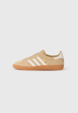 Beżowy sneaker Adidas z gumową podeszwą, białymi paskami po bokach i złotym tekstem "SAVILE" w pobliżu sznurowadeł, pokazany od zewnętrznej strony.