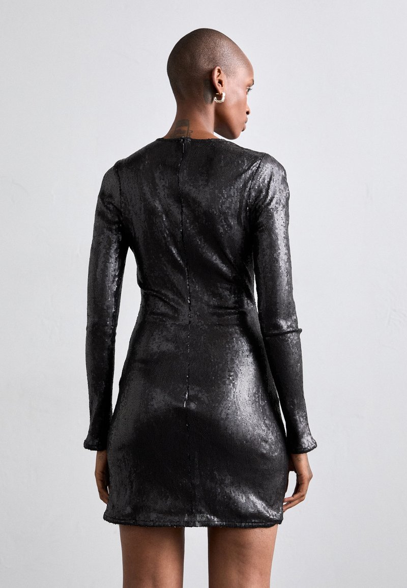 Robe mini en sequins noirs avec manches longues, design ajusté, texture lisse et détail de fermeture éclair au dos.