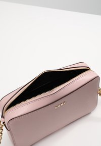 Borsa a mano in pelle rosa con chiusura a zip, dettagli in metallo dorato e tracolla a catena. Interno nero con una texture liscia. Il logo è impresso sulla parte anteriore.