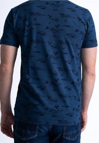 Mörkblå T-shirt med mönstrade mörka silhuetter av palmer, landskap och fjärilar. Kortärmad med rund halsringning.