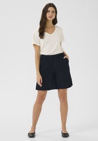 Navy blue, knee-length shorts with an elastic waistband and side pockets, paired with a cream V-neck T-shirt and black flat shoes.