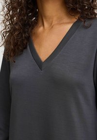 Mörkgrå långärmad topp med V-halsringning. Slät tyg med lätt glans. Har kontrasterande kant längs halsringningen.
