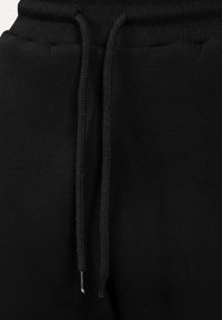 Schwarze Jogginghose mit einem Kordelzugbund, gerippter Textur und metallenen Enden an den Kordeln. Weicher Stoff in einer einfarbigen Ausführung.