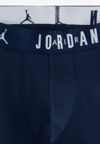Marineblå boxer briefs med en hvid elastisk talje, der har "JORDAN" og et gentaget logomønster. Blødt stof med en glat tekstur.