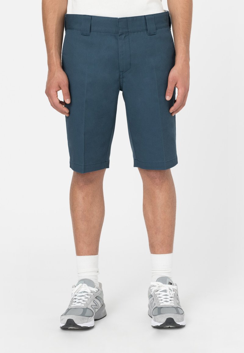 Shorts in cotone blu con vestibilità sartoriale, dotati di passanti per cintura e due tasche frontali. Indossati con sneakers grigie e calze bianche.