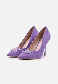 Escarpins à talons hauts en daim violet avec un embout pointu et une décoration métallique en forme de cœur. Intérieur lisse et talon aiguille élancé.