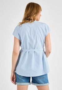 Top a maniche corte a righe blu chiaro e bianche con design peplum e vita con cintura, abbinato a pantaloni di jeans arrotolati.