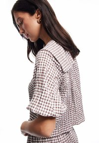 Karo-bluse in Braun und Weiß mit großem Kragen und kurzen, puffigen Ärmeln aus strukturiertem Stoff.