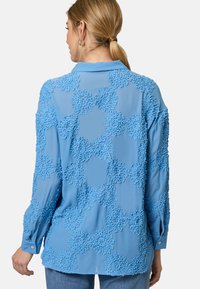 Light blue long-sleeve shirt featuring textured flower patterns; smooth fabric; pointed collar; buttoned cuffs; relaxed fit.