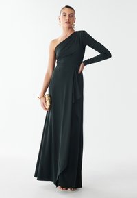 Eén-schouder, donkergroen avondjurk met een strakke bodice en een vloeiende rok. Kenmerkt zich door textuurstof en een zij-drape detail.