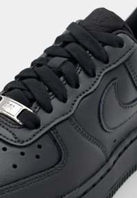 Svart lädersneaker med texturerad yta, med svarta snören och en silverfärgad ögla. Designen inkluderar perforerade detaljer och en söm i sulan.