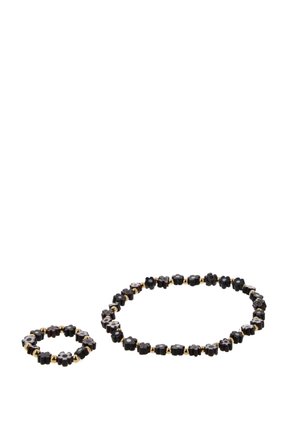 Fekete virág alakú gyöngy nyaklánc és hozzá illő karkötő fehér háttéren, kis arany távtartó gyöngyökkel.