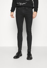 Jeans ajustados negros con una textura suave y un diseño ceñido. Combinados con un suéter negro que presenta texto gráfico blanco. Se complementan con zapatos negros.