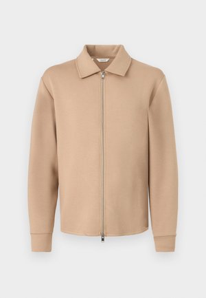 Veste beige à fermeture éclair avec col et manches longues, présentée sur un fond blanc uni.