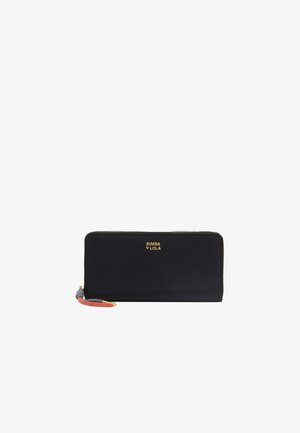 Cartera negra con un acabado de tela suave, logotipo dorado en el centro, cierre de cremallera y una correa de muñeca multicolor. Forma rectangular.