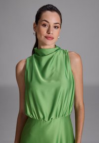 Grünes satinloses ärmelloses Kleid mit U-Ausschnitt und elastischem Bund. Glatte Textur, leichter Glanz und minimalistisches Design.