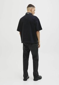Camiseta negra de manga corta con un corte relajado, combinada con jeans negros y zapatos negros. Diseño minimalista, sin patrones o logotipos visibles.
