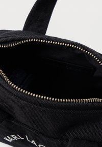 Μαύρη τσάντα υφάσματος με ασημένιο φερμουάρ ανοιχτή εν μέρει, αποκαλύπτοντας κενό εσωτερικό και μία λαβή προσαρτημένη στο επάνω μέρος.