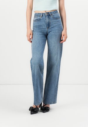 Jean large taille haute en denim bleu clair, avec un design classique à cinq poches et un léger effet délavé, accompagnés de chaussures à talons noires.