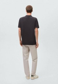 Tummanharmaa polo-paita lyhythihaisena, esiteltynä takaa, yhdessä vaaleanbeigejen housujen ja valkoisten lenkkarien kanssa. Sileä kangas.