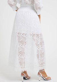 Witte lange rok met ingewikkelde uitgesneden patronen, een smockband en kanten afwerking aan de zoom. Gecombineerd met witte gekruiste hakken.