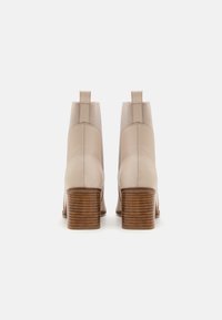 Beige Leder-Stiefeletten mit glatter Oberfläche, elastischen Seitenpaneelen und einem strukturierten braunen Blockabsatz. Schlichtes, modernes Design.