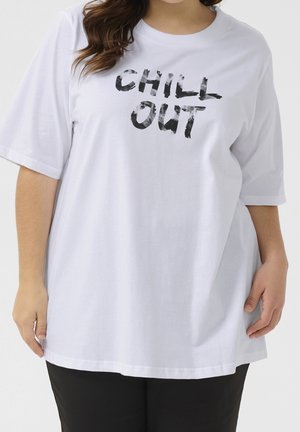 White oversized T-shirt with black worn-style text "CHILL OUT" worn by a person with hands relaxed at sides.