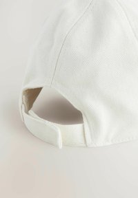 Cappellino da baseball bianco in cotone con superficie testurizzata, visiera curvata e cinturino regolabile sul retro. Le cuciture sono visibili.