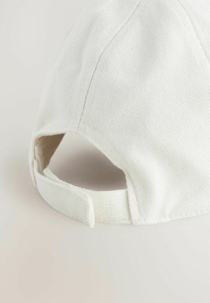 Valkoinen puuvillainen baseball-lippis, jossa on teksturoitu pinta, kaareva lippa ja säädettävä hihna takana. Ompeleet ovat näkyvissä.