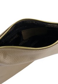 Beige lædertaske indvendig med gylden lynlås. Den sorte foring har et gentaget brand-mønster. En enkelt indvendig lomme er synlig.