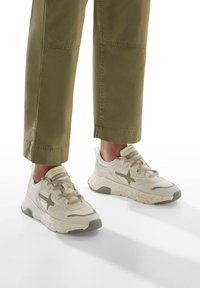 Sneakers beige chiaro con tomaia strutturata, caratterizzati da una stella di un beige più scuro e una suola maculata. I lacci sono piatti e coordinati con il colore.