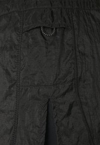 Černá texturovaná látka s kapsou vybavenou elastickým šňůrkovým tahem. Obsahuje vertikální štěrbinu u dolní části.