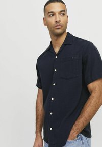 Marineblauwe korte mouwen knoopshirt van textuurstof, met een zak en lichtgekleurde knopen. Geborduurd detail op de zak.
