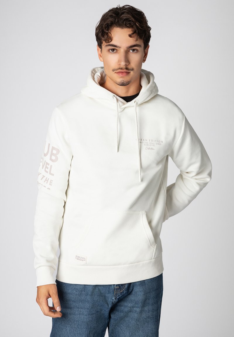 White hooded sweatshirt with a front pocket, featuring light beige text on the left sleeve and chest. Made of soft fabric with a relaxed fit.