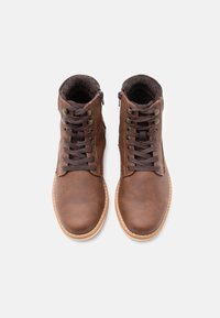 Ruske nahkasaapad nilkkoihin, jolla on sileä pinta, pyöreä varvas, nauhakiinnitys edessä ja sivuvetoketju. Vaaleanruskea pohja, jossa on ommeltu yksityiskohtia.