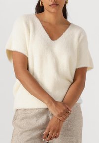 Witte, korte mouwen, V-hals trui gemaakt van zachte, pluizige stof. Gekocht over een getextureerde, metallic gouden rok met een geometrisch patroon.