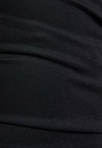Musta kangas, jossa on sileä tekstuuri, hienovaraisia kimaltelevia yksityiskohtia ja laskoksia, esittelee tyylikästä, modernia muotoilua.