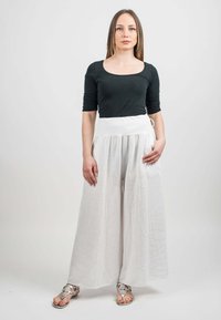 Svart långärmad topp i kombination med lätta, vita vida byxor som har fickor och knytning i midjan. Silverfärgade dekorativa sandaler fulländar looken.
