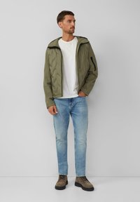 Zielona pikowana kurtka z kapturem, zapinana na suwak z przednią i boczną kieszenią; noszona na białej koszulce i jasnoniebieskich dżinsach, w zestawie z brązowymi botkami.