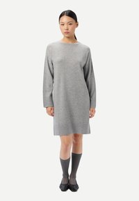 Robe en maille grise à manches longues avec un col rond, coupe ample et texture douce, assortie à des chaussettes grises montant jusqu'aux genoux et à des chaussures noires.