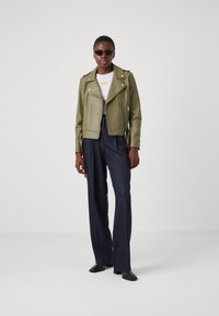 Jachetă de biker din piele verde, cu elemente din metal argintiu, combinată cu pantaloni navy cu talie înaltă și cizme negre până la glezne. Ochelarii de soare completează ținuta.