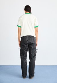 Camisa creme de manga curta com acabamentos verdes, combinada com calças cargo pretas com bolsos com fecho éclair e cordões ajustáveis nos punhos.