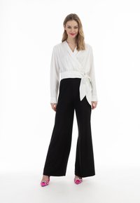Hvid indpakket bluse med en bundet detalje, kombineret med sorte vide bukser og rosa heels med dekorative sløjfer. Glat stof og skræddersyet pasform.