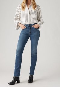 Randig skjorta i vitt och marinblått, tillsammans med åtsittande mörkblå jeans och svarta klackstövlar, som visar en stilren och skräddarsydd look.