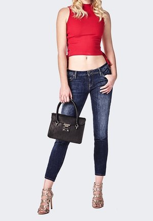 Top corto rojo con textura acanalada, jeans de denim oscuro, sandalias de tacón plateadas y un bolso negro texturizado con detalles de herrajes. Enfoque claro en el diseño del atuendo.