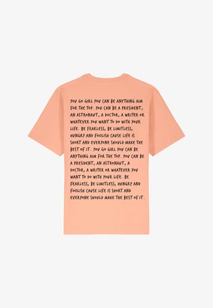 Perzikkleurig t-shirt met korte mouwen met zwarte tekst op de achterkant, voorzien van motiverende zinnen over ambitie en zelfvertrouwen.